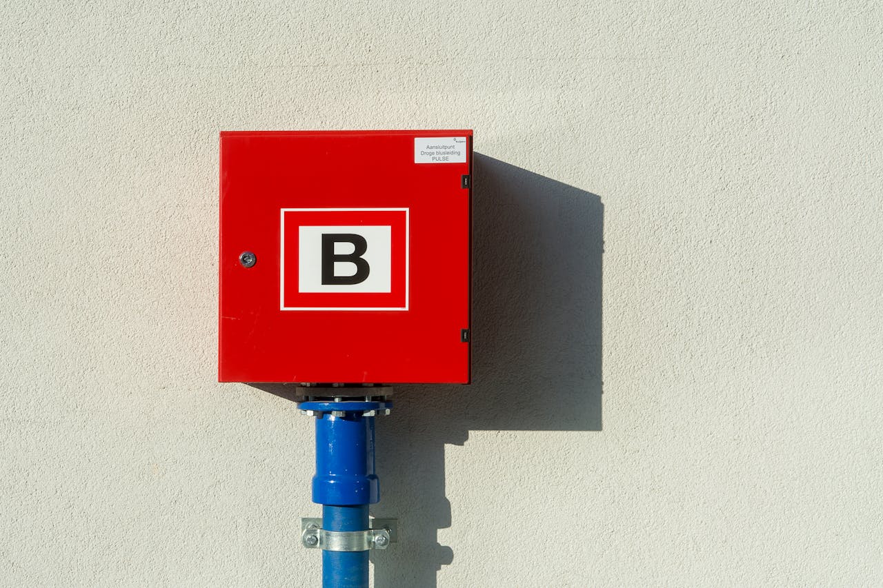 Red emergency box mounted on sunlit wall casting a shadow.